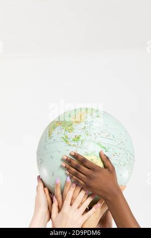 A large globe with all continents is supported by female hands of various races, symbolizing unity, acceptance and racial tolerance. Stock Photo