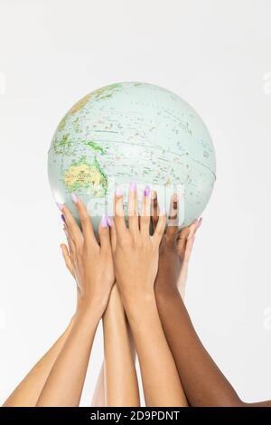 A large globe with all continents is supported by female hands of various races, symbolizing unity, acceptance and racial tolerance. Stock Photo