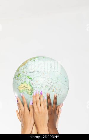 A large globe with all continents is supported by female hands of various races, symbolizing unity, acceptance and racial tolerance. Stock Photo