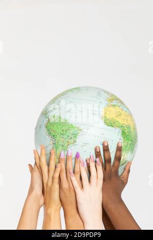 A large globe with all continents is supported by female hands of various races, symbolizing unity, acceptance and racial tolerance. Stock Photo