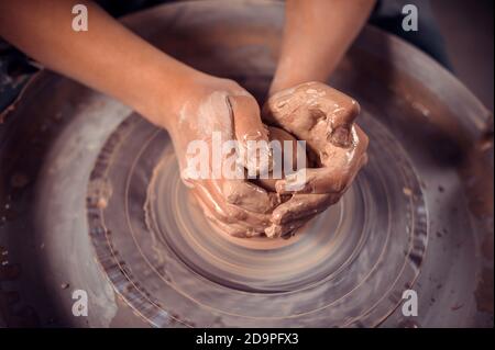 The potter's hands are shaped a cup from a clay. The process of creating pottery on a potter's wheel. The master ceramist works in his studio. Close Stock Photo