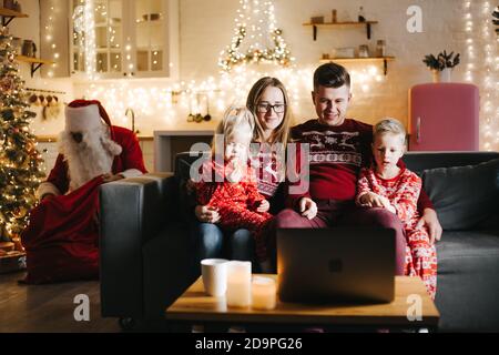 Santa Claus putting gifts under Christmas tree in room with family Stock Photo