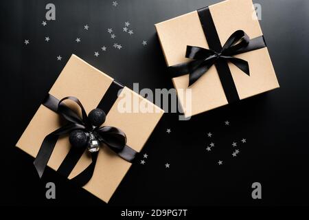 Luxury Christmas gift boxes with ribbon bow on black background with confetti. Xmas presents, New Years surprises. Flat lay, top view. Stock Photo