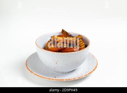 Bright orange grilled pumpkin in a white bowl on a white background. Autumn harvest. Copy space. Selective focus. Horizontal orientation. Stock Photo