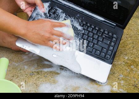 closeup cleaning computer notebook with dish washing soap, technology concept Stock Photo