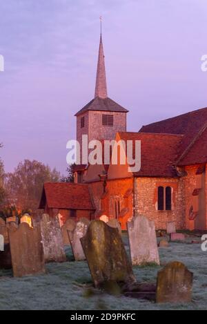 St Laurence and All Saints Church in Eastwood, Southend on Sea, Essex, UK, at dawn with warm glow. Grave headstones