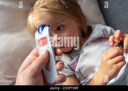 Parent takes temperature for her child with infrared thermometer at home, high fever Stock Photo