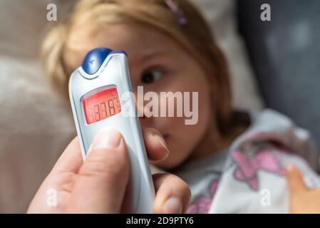 Parent takes temperature for her child with infrared thermometer at home, low-grade fever Stock Photo