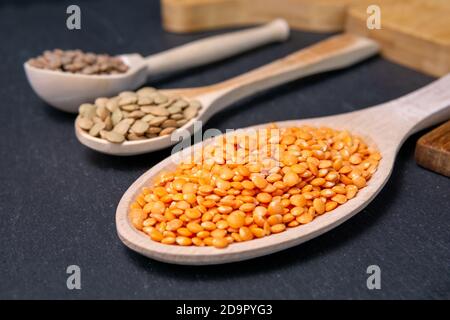 dry orange, red, green lentils in wooden spoons on a black background top view, flat lay Stock Photo