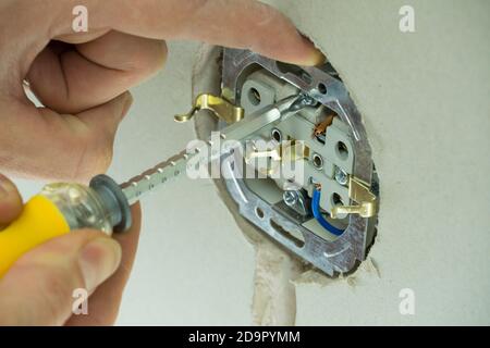 Electrician connects the sockets to the electrical wires. Installation wire into a plug. A man installs an electrical outlet in the wall. Close up of Stock Photo