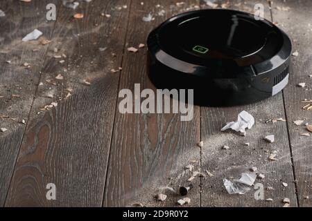 Balck robotic vacuum cleaning wooden floor from dust and rubbish Stock Photo