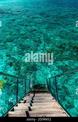 Jetty over swimming atoll and a tropical resort island in Maldives ...
