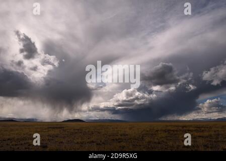 Amazing view of stormy sky with clouds, thunderclouds and rain over snowy mountains in steppe Stock Photo