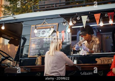 afro-american employee showing size of a fast food mealto a caucasian customer from a window of modified truck for mobile fast food Stock Photo