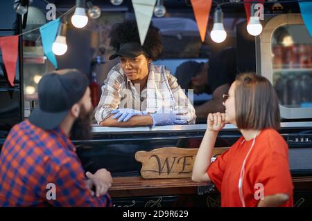 afro-american female employee in fast food service looking at male customer with smile, listening Stock Photo