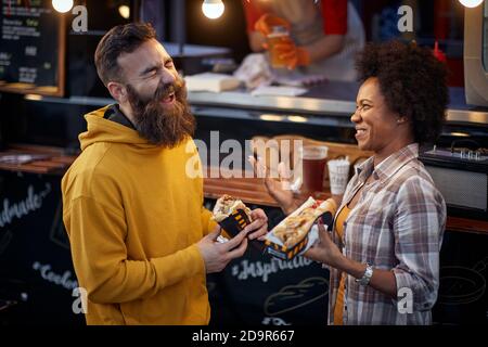 multiethnic couple laughing out loud, having a good time, talking, eating sandwiches Stock Photo