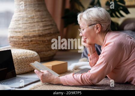 Senior woman relaxing on floor at home reading book. Stock Photo