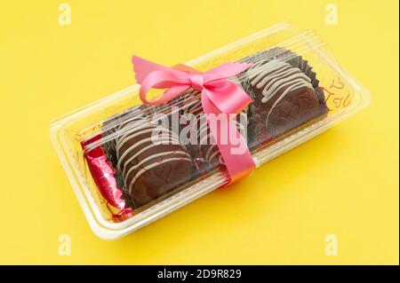 Delicious homemade chocolate bonbon packed for gift with red ribbon. Isolated on yellow background. Copy space. Stock Photo
