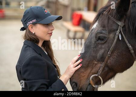 woman in cap petting horse Stock Photo