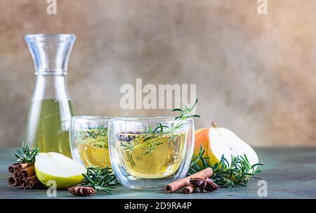 Spicy hot pear or apple cider with cinnamon, anise and rosemary. Traditional autumn or winter drinks. Green concrete background. Selective focus. Stock Photo