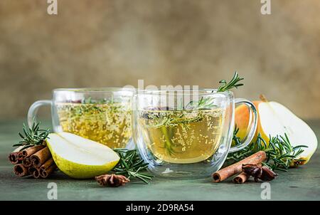 Spicy hot pear or apple cider with cinnamon, anise and rosemary. Traditional autumn or winter drinks. Green concrete background. Selective focus. Stock Photo