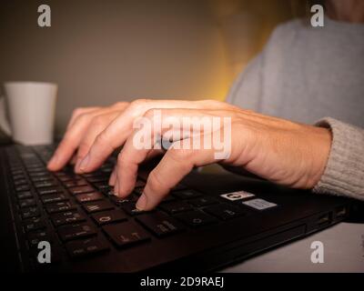 Closeup of a woman typing on a laptop and working from home at night Stock Photo