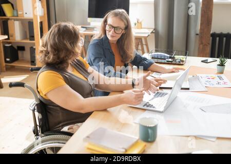 Two young female office managers sitting by table and discussing working points Stock Photo
