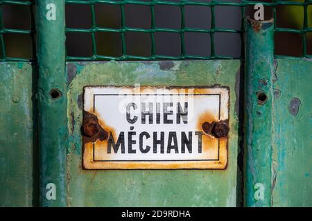 Rusty warning sign written in French saying "Nasty dog" on an old worn green gate Stock Photo