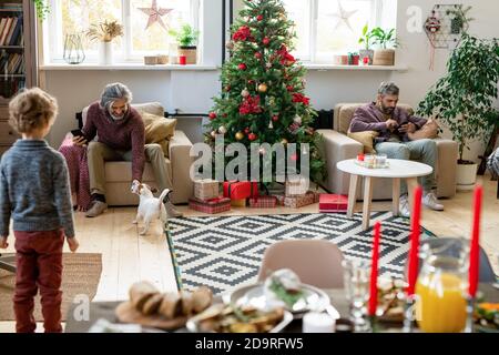 Senior man with smartphone playing with dog while his son using mobile gadget Stock Photo