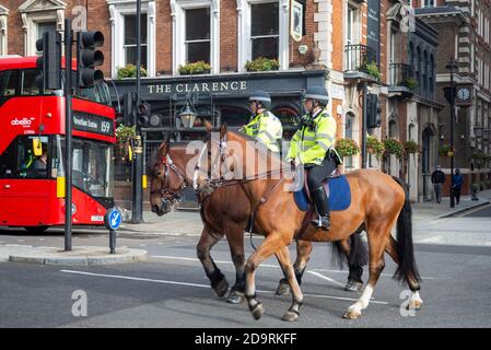 British mounted police officers in Whitehall, Westminster, London, UK, riding past a pub and a red London bus. English police in London on horses Stock Photo