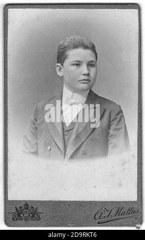 Vintage cabinet card shows portrait of the young man wearing bow tie. Photo was taken in a photo studio. Edwardian era. Photo was taken in Austro Stock Photo