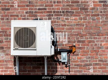 An air conditioning unit on an old brick wall. Cable and hoses run into the wall through a hole with insulation. There is room for text. Stock Photo