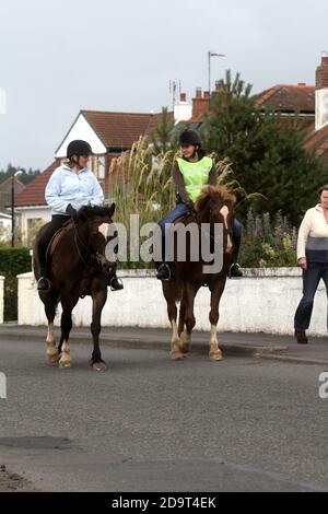 Maidens Harbour, South Ayrshire, Scotland, UK . Maidens is a village in the Kirkoswald parish of Ayrshire, Scotland. Situated on the coast of the Firth of Clyde at the southern end of Maidenhead Bay, a series of rocks known as the 'Maidens of Turnberry' form a natural harbour.  Two horse riders on the prmenade head back to the riding school Stock Photo