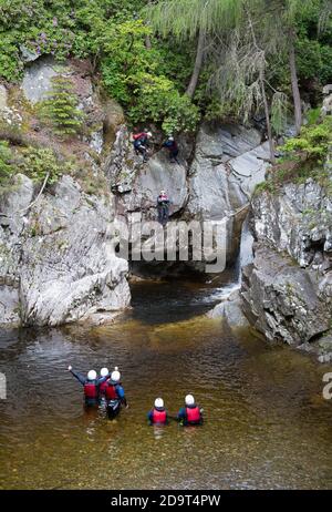 People abseiling down rockface and into a pool under the Falls of Bruar, Perthshire, Scotland, UK. Stock Photo