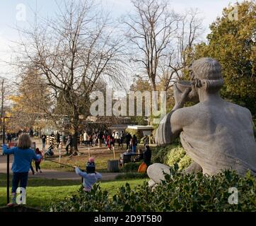 Mark Batten’s sculpture “The Diogenist”. A statue overlooking a crowded Golders Hill Park with children playing in the foreground. Stock Photo