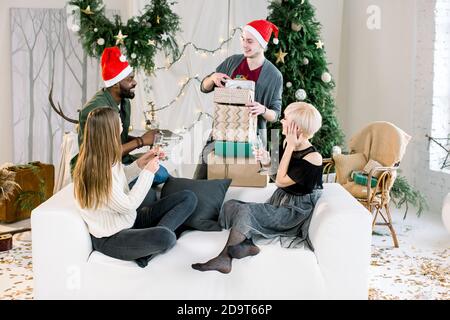 family, Christmas, holidays, happiness and people concept- happy four multiethnical friends sharing Christmas gifts Stock Photo