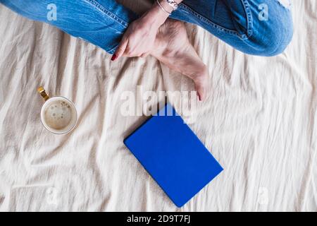 Girl sitting on the floor on a blanket with a mug of coffee and a notepad, top view. The girl writes down her ideas Stock Photo