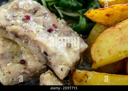 Detail on a plate based on cod with pink pepper, baked potato wedges and valerian Stock Photo