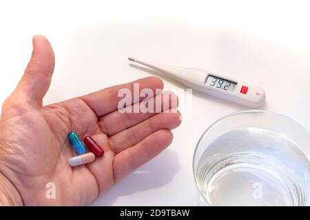 digital thermometer showing fever values, hand holding tree pills and water glass Stock Photo