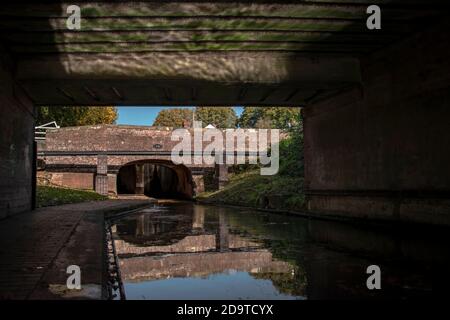 a old bridge taken from under a bridge with the reflection of the water on the top of the bridges roof with the canal below Stock Photo