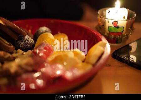 Black cellphone lying offline on a wooden table, with candlelight and pastry in a red plate on christmas eve. Blurry background for concepts. Stock Photo