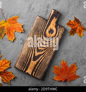 Handcrafted old wooden cutting board with autumn leaves on concrete background, top view Stock Photo