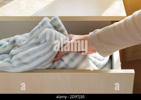 Woman hand pulls out a striped fuzzy blanket from the chest of drawers in a room. Warm fleece bedding for coziness and comfort in the winter season. Stock Photo