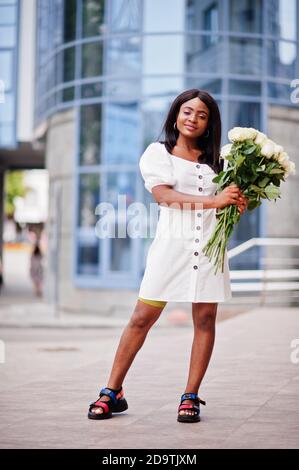 Beautiful african american girl holding bouquet of white roses flowers on dating in the city. Black businesswoman with bunch of flowers. Stock Photo