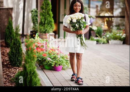 Beautiful african american girl holding bouquet of white roses flowers on dating in the city. Black businesswoman with bunch of flowers. Stock Photo