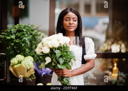 Beautiful african american girl holding bouquet of white roses flowers on dating in the city. Black businesswoman with bunch of flowers. Stock Photo