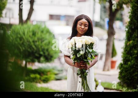 Beautiful african american girl holding bouquet of white roses flowers on dating in the city. Black businesswoman with bunch of flowers. Stock Photo