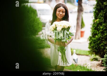 Beautiful african american girl holding bouquet of white roses flowers on dating in the city. Black businesswoman with bunch of flowers. Stock Photo