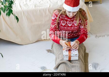 Woman in Santa hat wrapping modern Christmas gifts presents at home. Holidays New Year and Christmas concept. Stock Photo