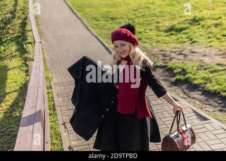 A happy woman walks up the stairs in burgundy palette and biret, an adult with beautiful eyes in black clothes, in the fall against the background of Stock Photo